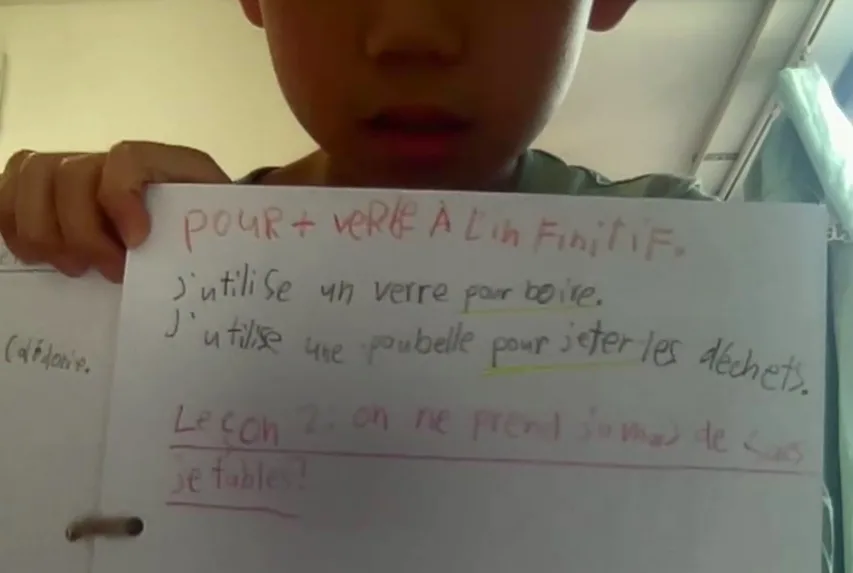 A non-French-speaking child showing a slate with French sentences, illustrating sentence structure and learning French for bilingual children.