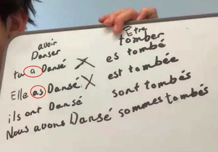 A bilingual child showing a slate with two French verbs difficulties in passé composé, practicing French conjugation and learning French for non-French-speaking children. 